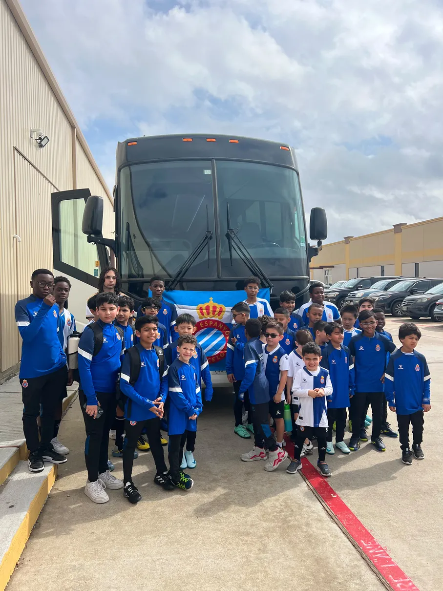 RCDE Academy Texas squad posing with the Espanyol flag in front of the team bus before a tournament trip
