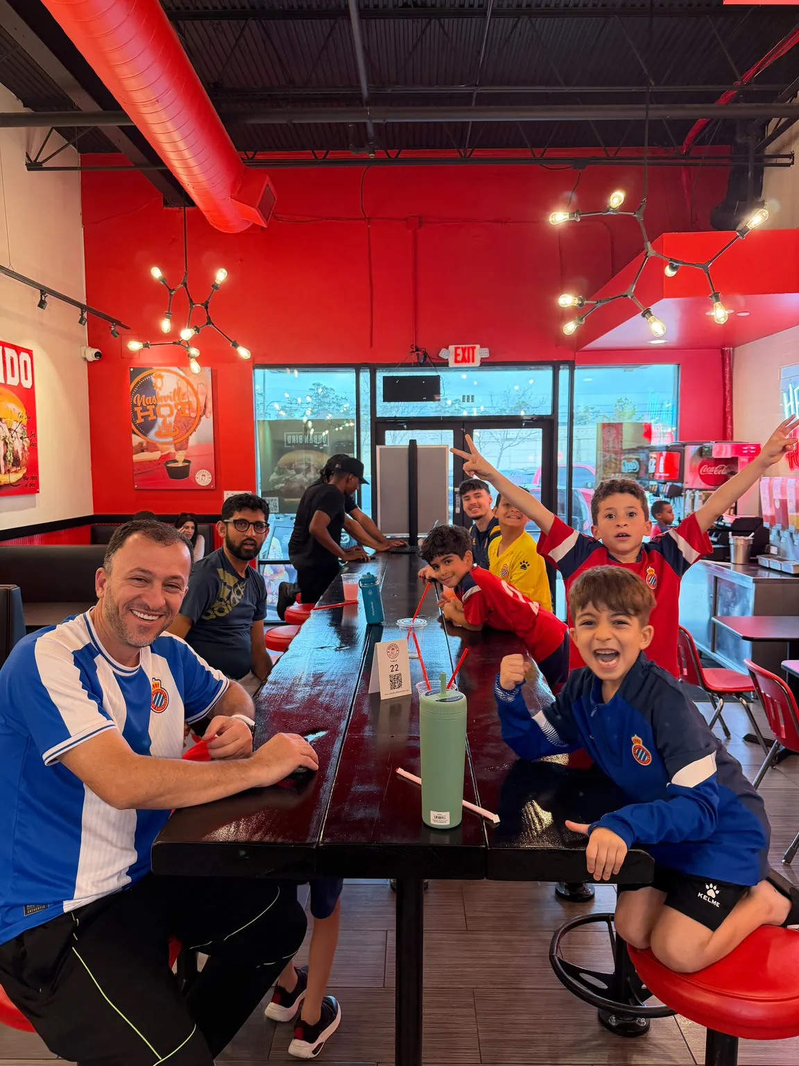 Coach and academy players celebrating with peace signs at a hot chicken restaurant after a match