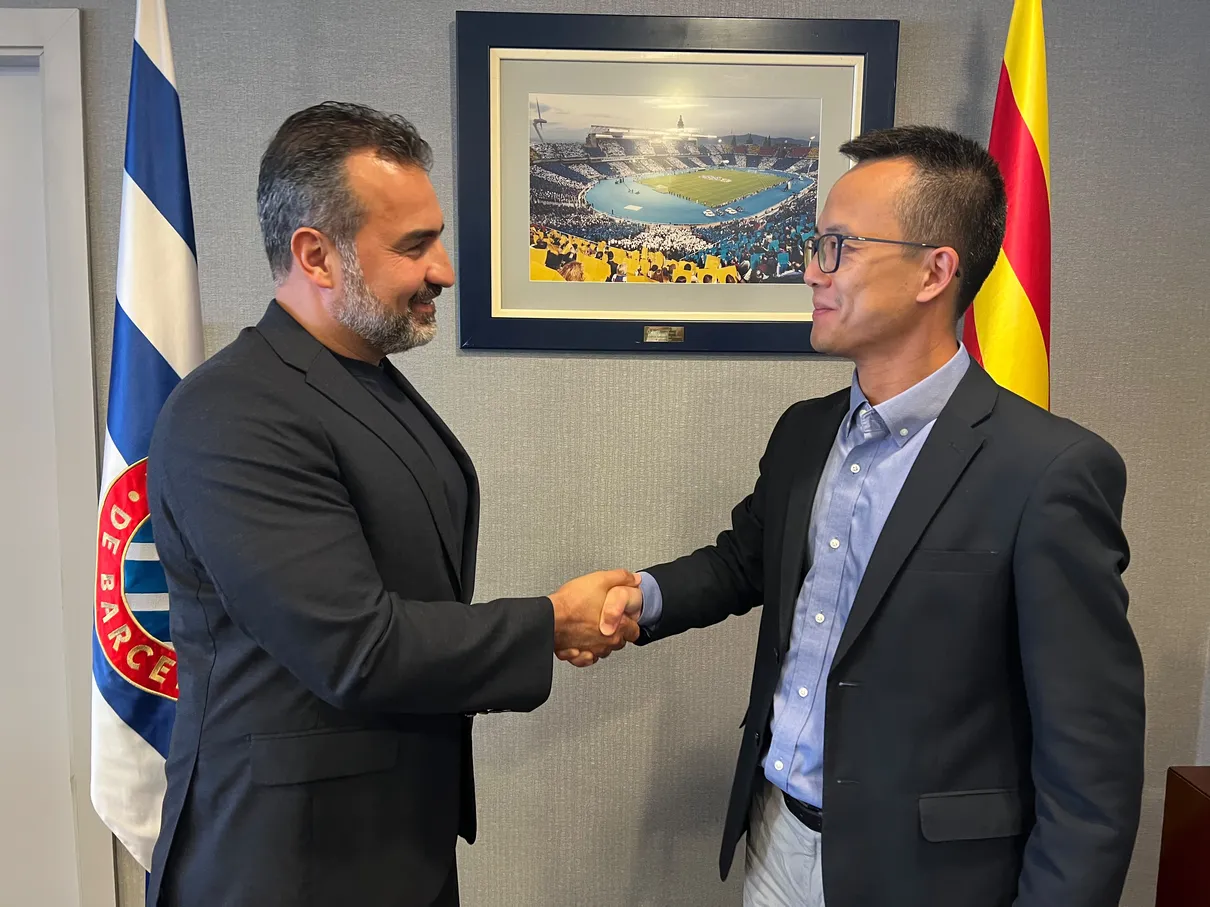 RCDE Academy Texas director shaking hands with RCD Espanyol leadership in front of a framed Stage Front Stadium photo