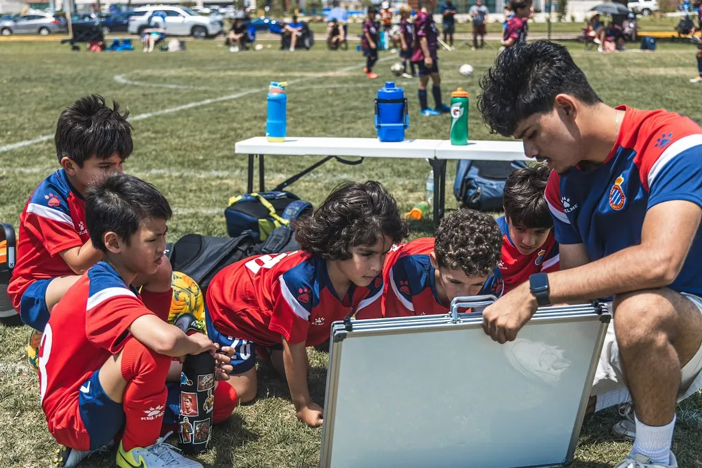 Coach showing tactics board to kneeling players on the field